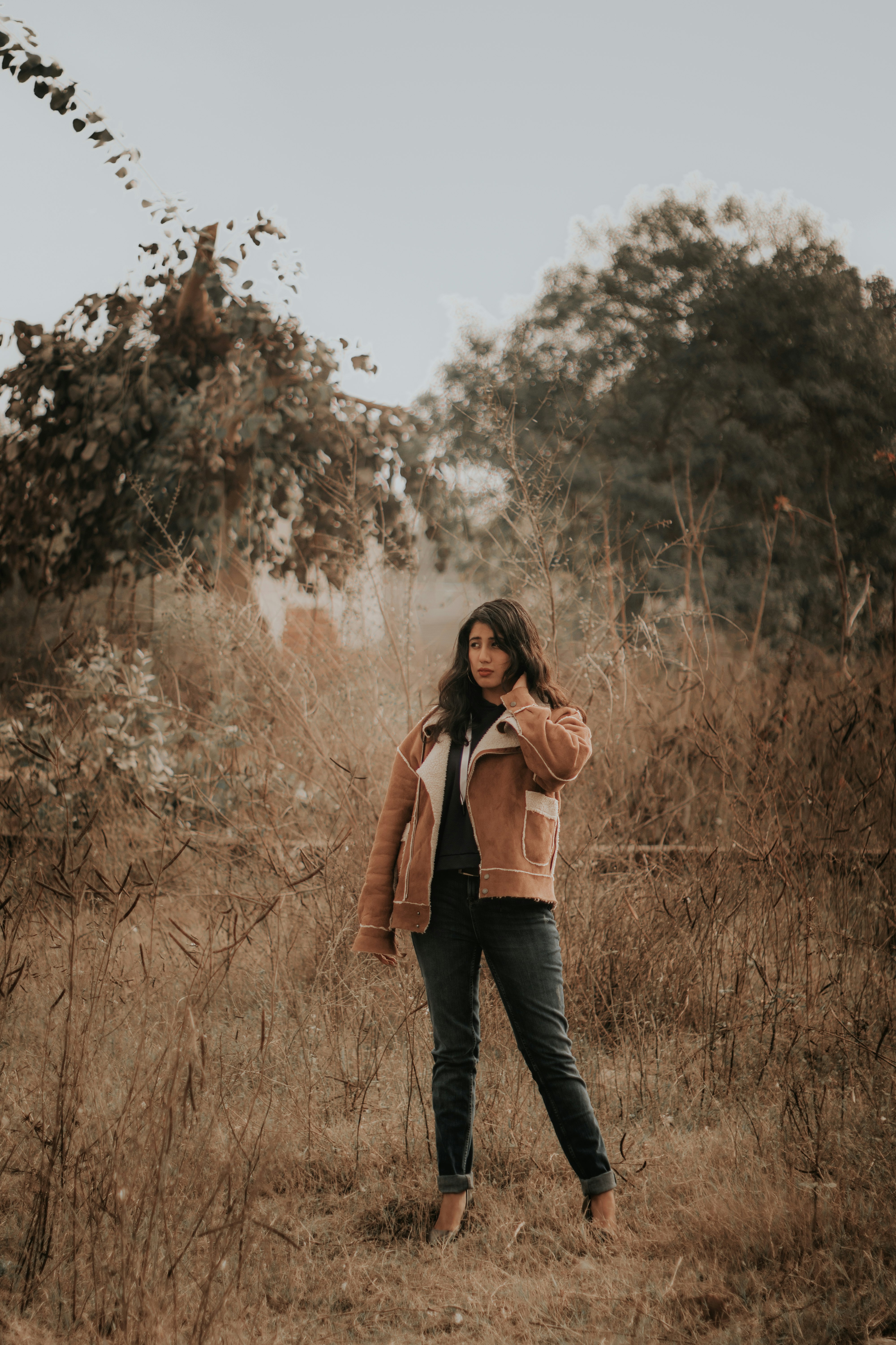 woman in brown coat standing on brown grass field during daytime